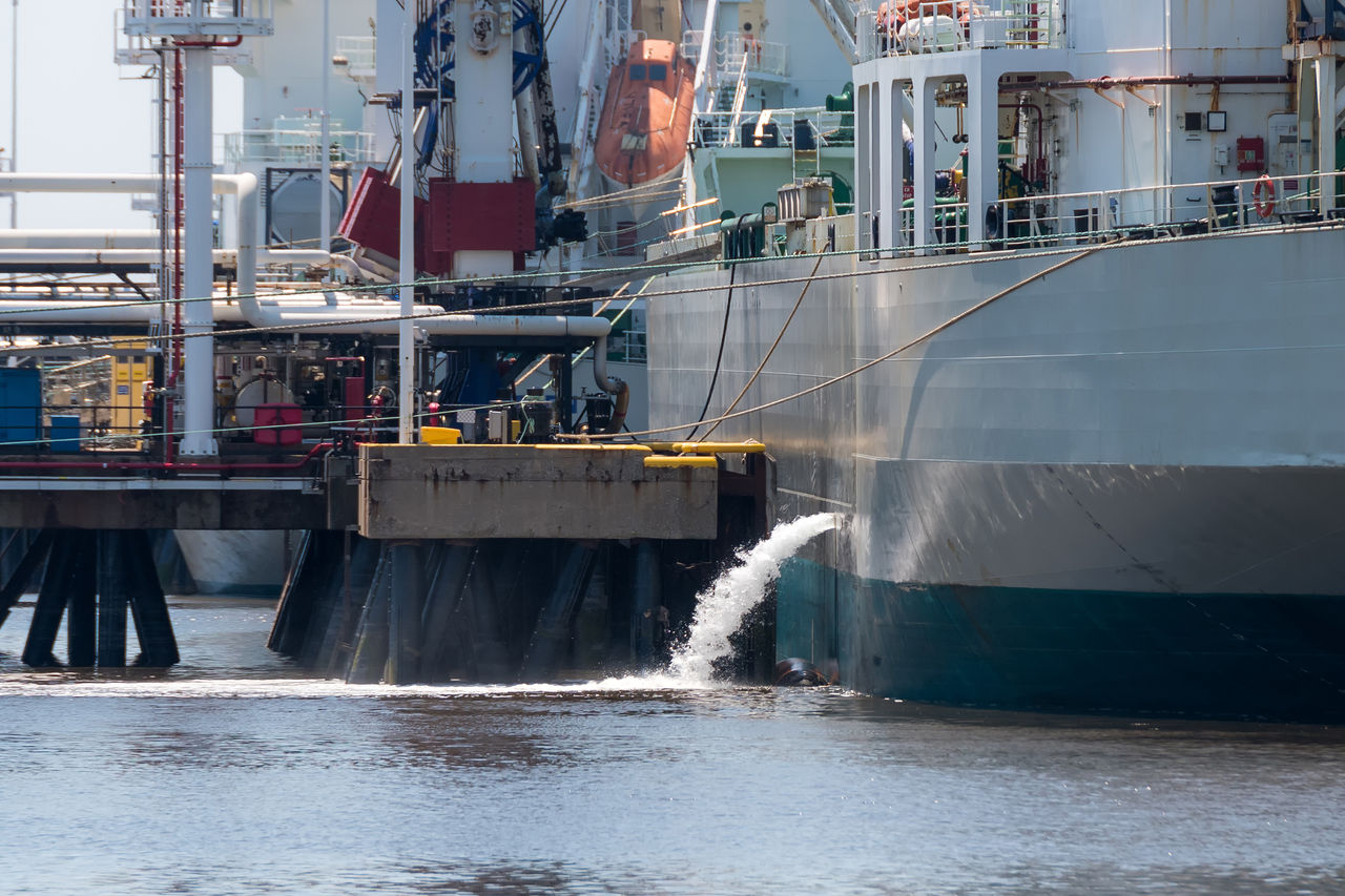 A tanker discharging ballast. The ship is docked at a pier. Lots of piping and machinery on the dock