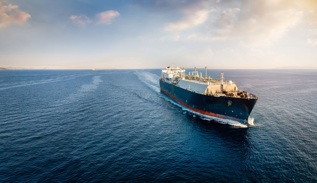 Front view of a big LNG tanker ship traveling with full speed over the ocean during sunset with copy space
