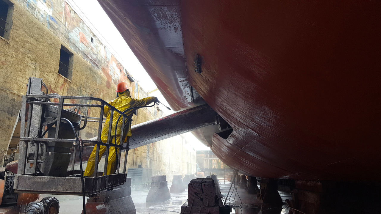 worker washing ship hull at drydock,,~~~~~~~~~~~~~~~~~~~~~~~~~~~,,hardhat (PPE) added to this image. See related image for original image.