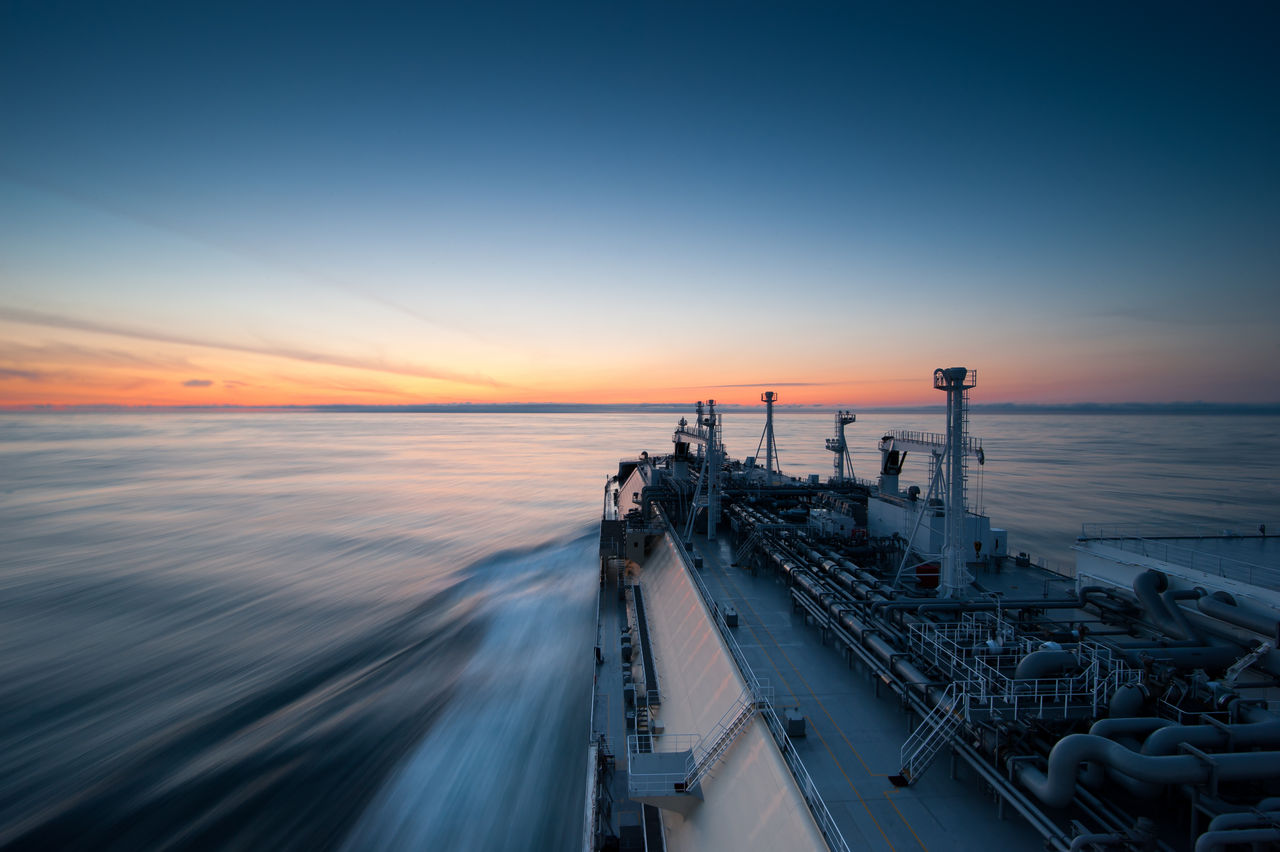 Liquigied natural gas tanker sails towards the sunset. Long exposure photo. Sun Light reflections are on the water. Blue sky with beautiful sunset sky and colors.